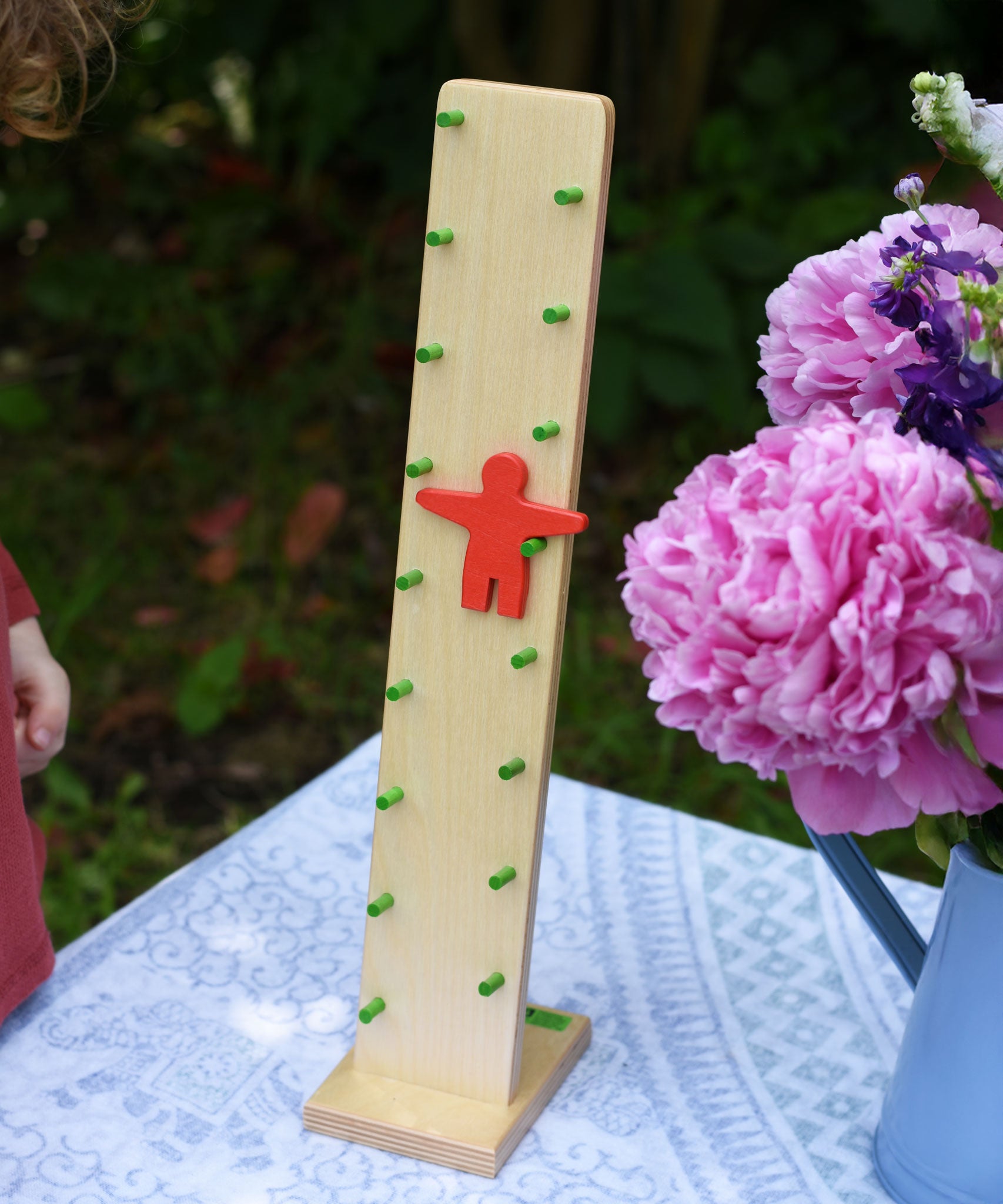 The Beck Toys Wobbler placed on a small table outdoors. The red figure can be seen in motion tumbling down the green coloured rungs. 