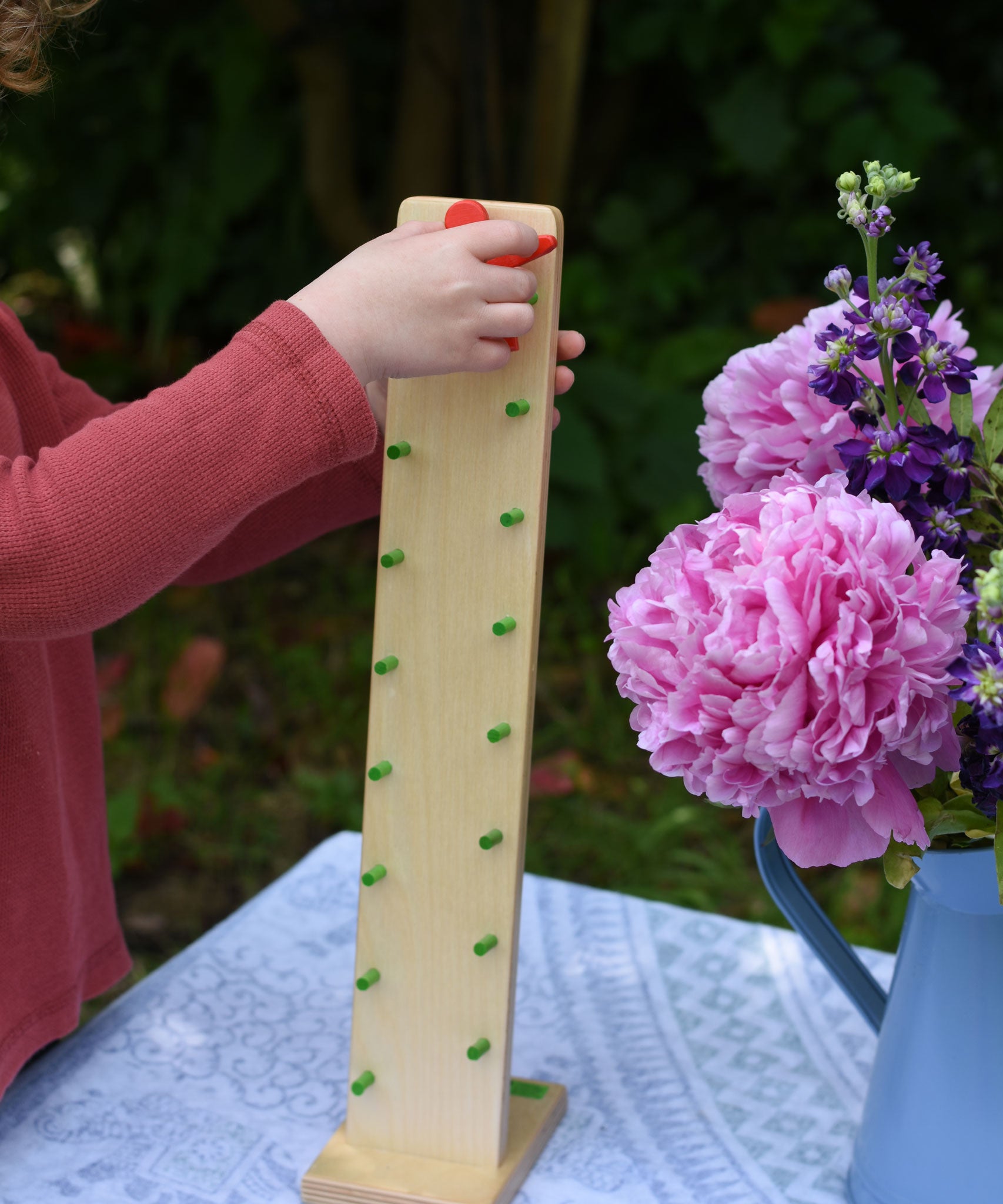A close up of a child's hand placing the red coloured figure on the Beck Toys wooden Wobbler tumbling toy.