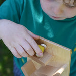 A close up of a child placing a yellow coloured race car on teh track of the Beck Toys Beechwood Cascading ‘Tower Running Track’ with Race Cars set. 