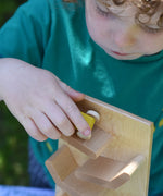 A close up of a child placing a yellow coloured race car on teh track of the Beck Toys Beechwood Cascading ‘Tower Running Track’ with Race Cars set. 