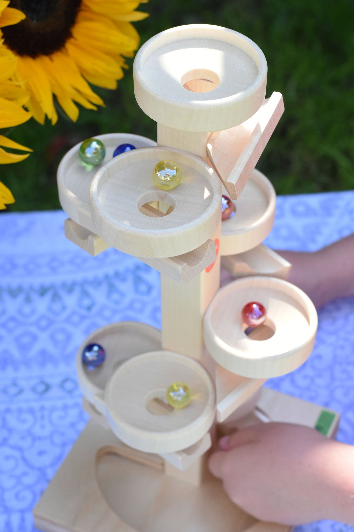 A top down view of the Beck Marble Run Plate Tower, a child's hands can be seen lifting marbles off the base. 