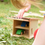 Beck wooden double garage toy with two toy cars inside, a child is pushing the door down to close it.