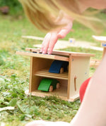 Beck wooden double garage toy with two toy cars inside, a child is pushing the door down to close it.