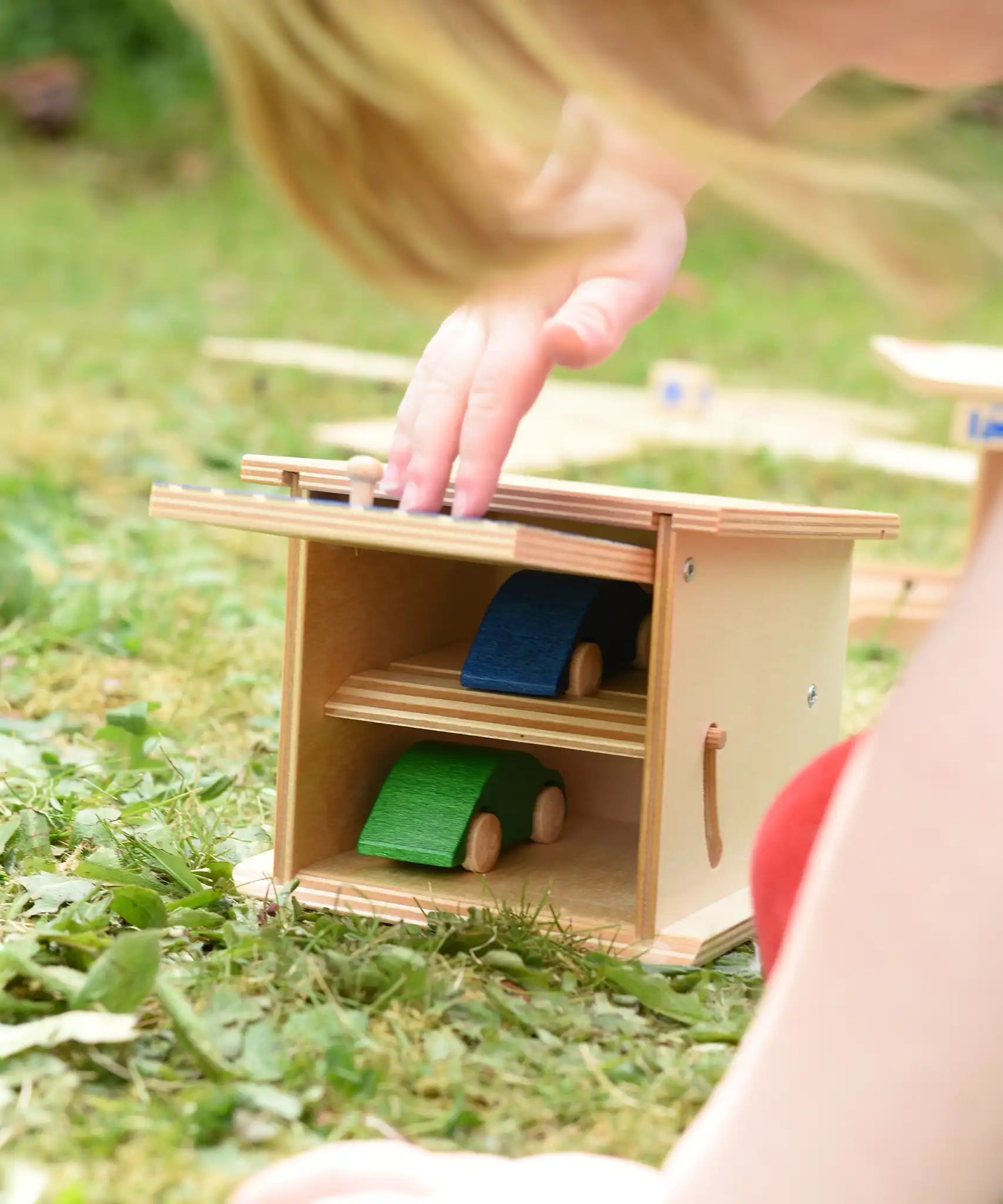 Beck wooden double garage toy with two toy cars inside, a child is pushing the door down to close it.