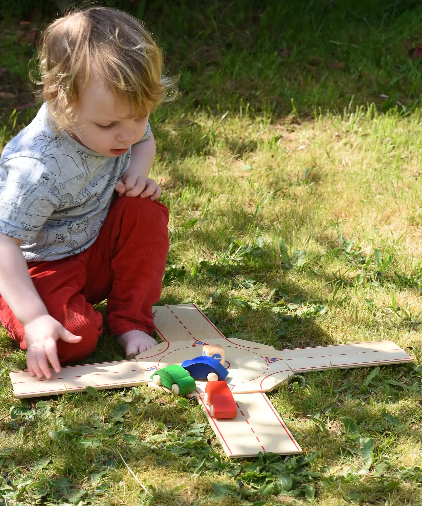 Child playing with the Beck wooden roundabout junction set, placing toy cars onto the road. 