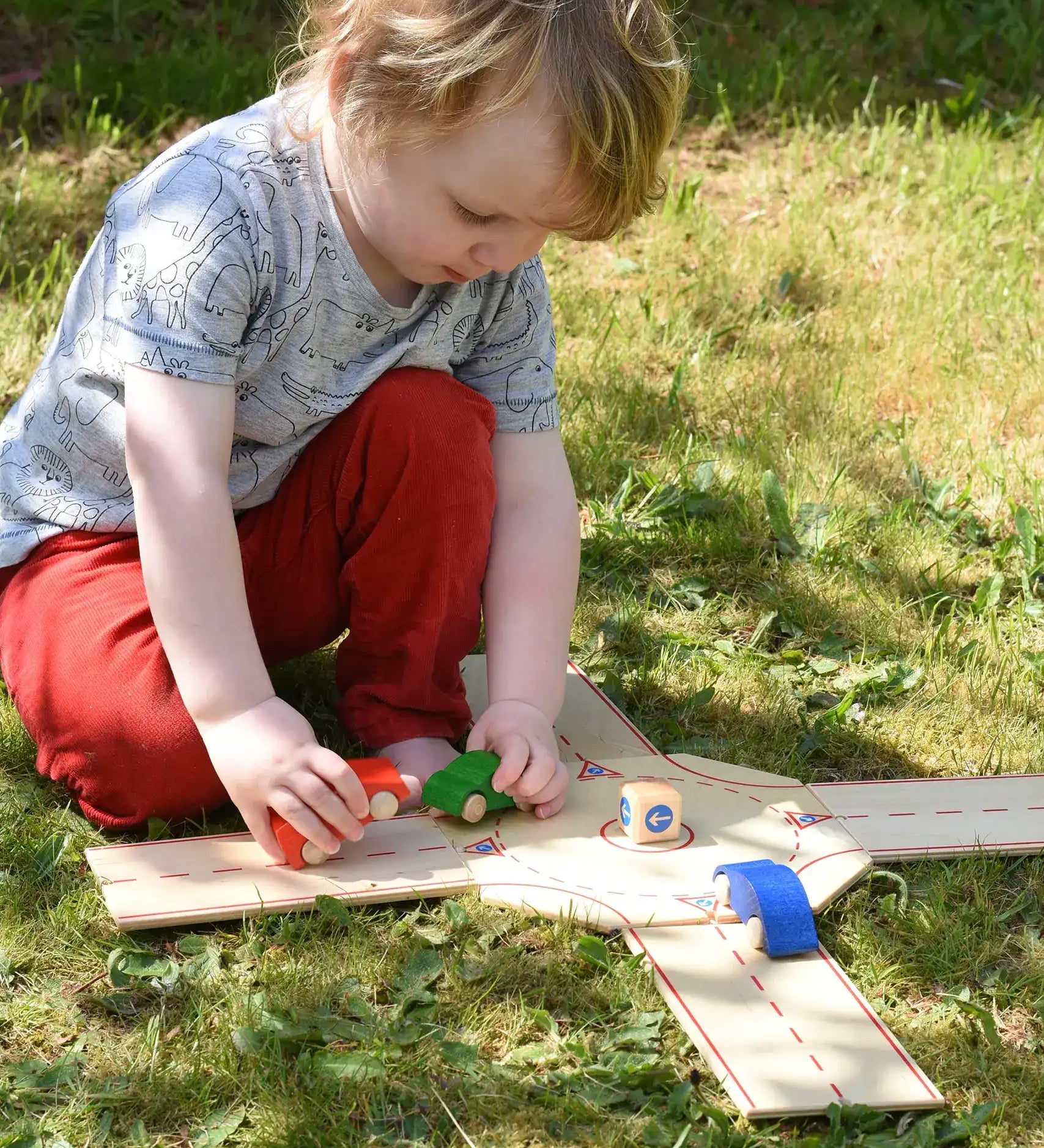 Child playing with the Beck wooden roundabout junction set, placing toy cars onto the road. 