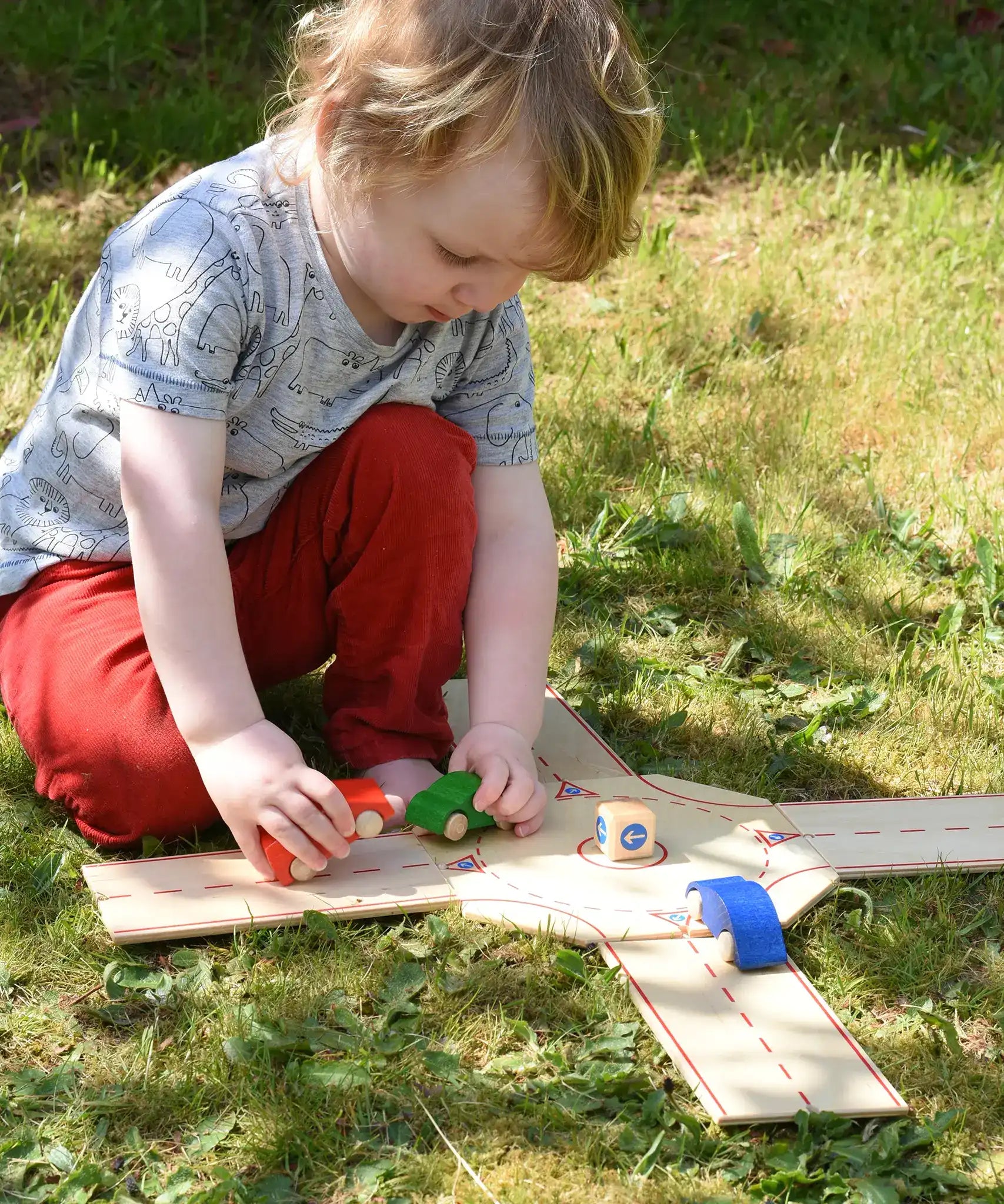 Child playing with the Beck wooden roundabout junction set, placing toy cars onto the road. 