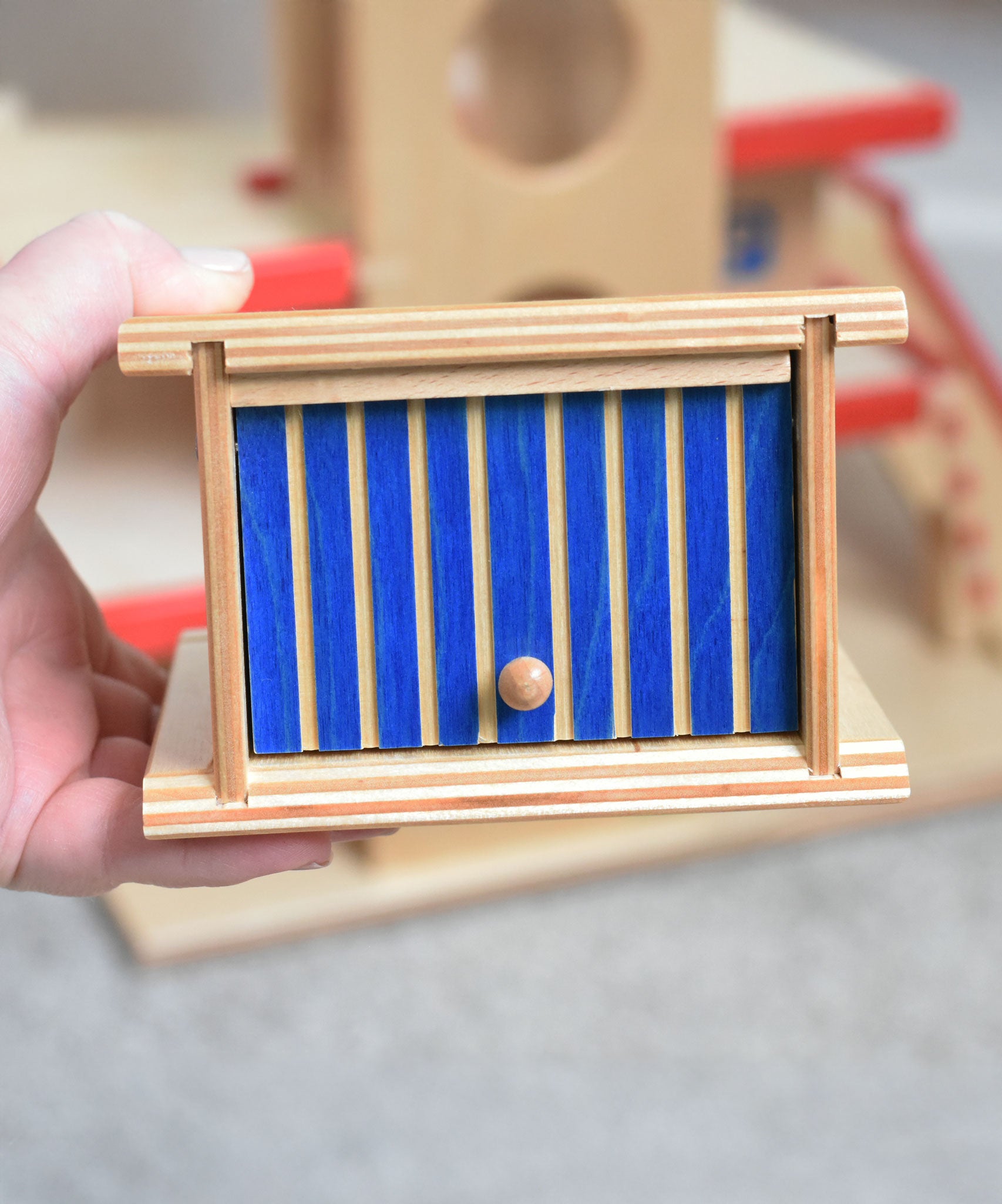 A Beck wooden toy car garage shown in an adult's hand. This wooden toy car garage is part of a wide range of toy vehicles and accessories available at Babipur.