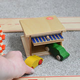 A Beck wooden toy car garage with a green coloured car half way in and a yellow one just outside. Beck have a range of wooden toys and ball runs available at Babipur. 