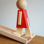 A side view of the wooden walking figure standing on the end of the track from the Beck Toys Nurmi Ramp Walker Wooden Toy Set.