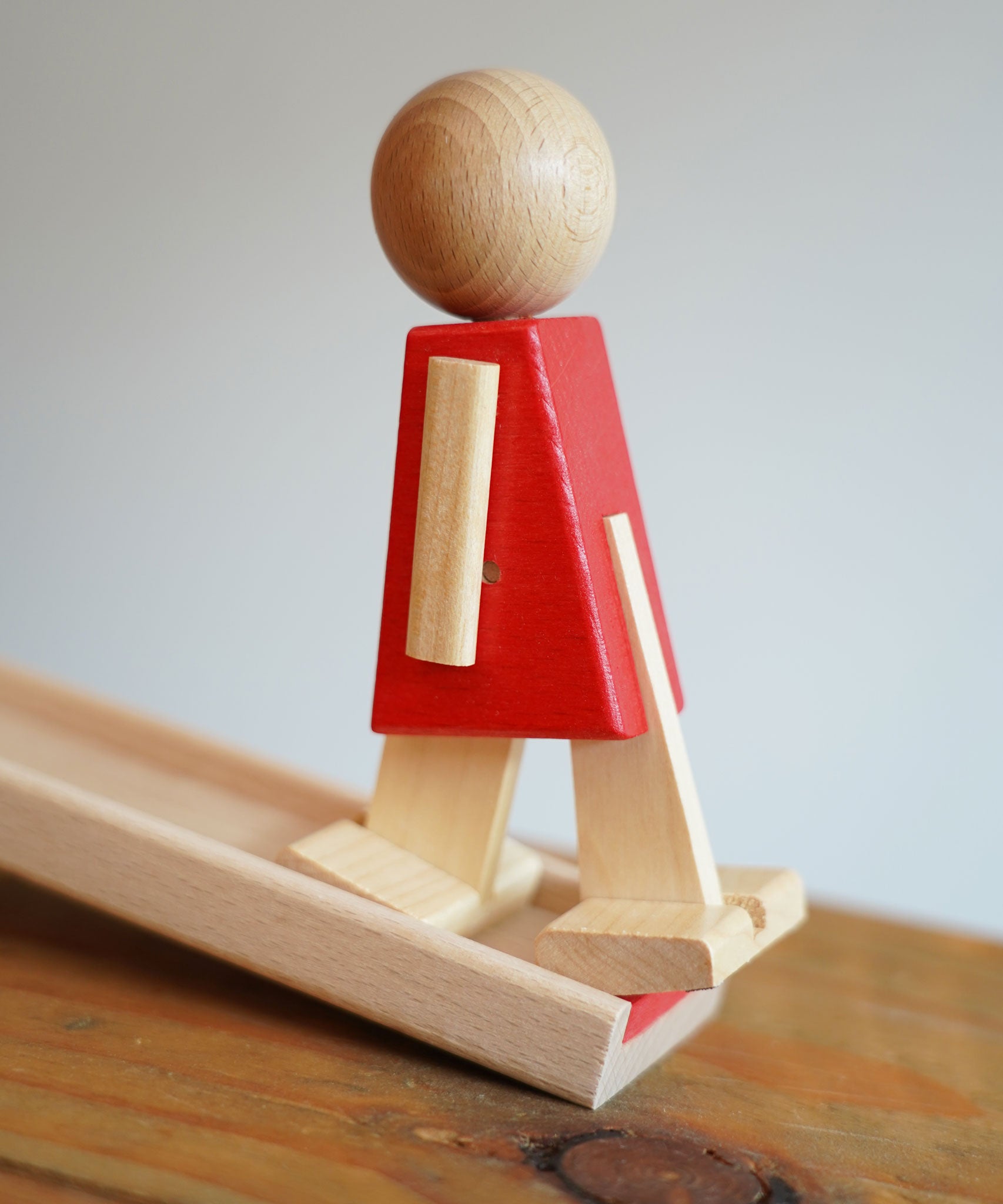 A side view of the wooden walking figure standing on the end of the track from the Beck Toys Nurmi Ramp Walker Wooden Toy Set.