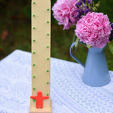 Beck wooden toys Wobbler tumbling toy with Red Figure placed on a small covered table. A bunch of flowers can be seen in the background. 