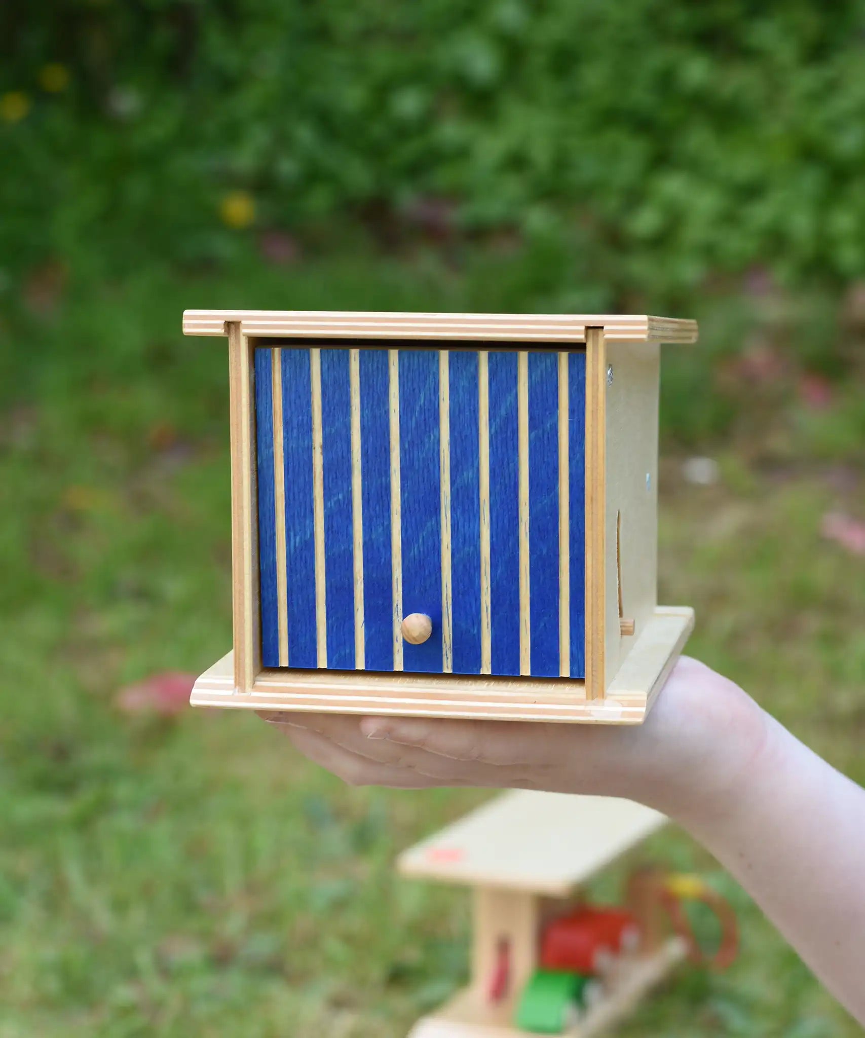 Beck wooden double garage toy in a child's hand. The blue door is closed.