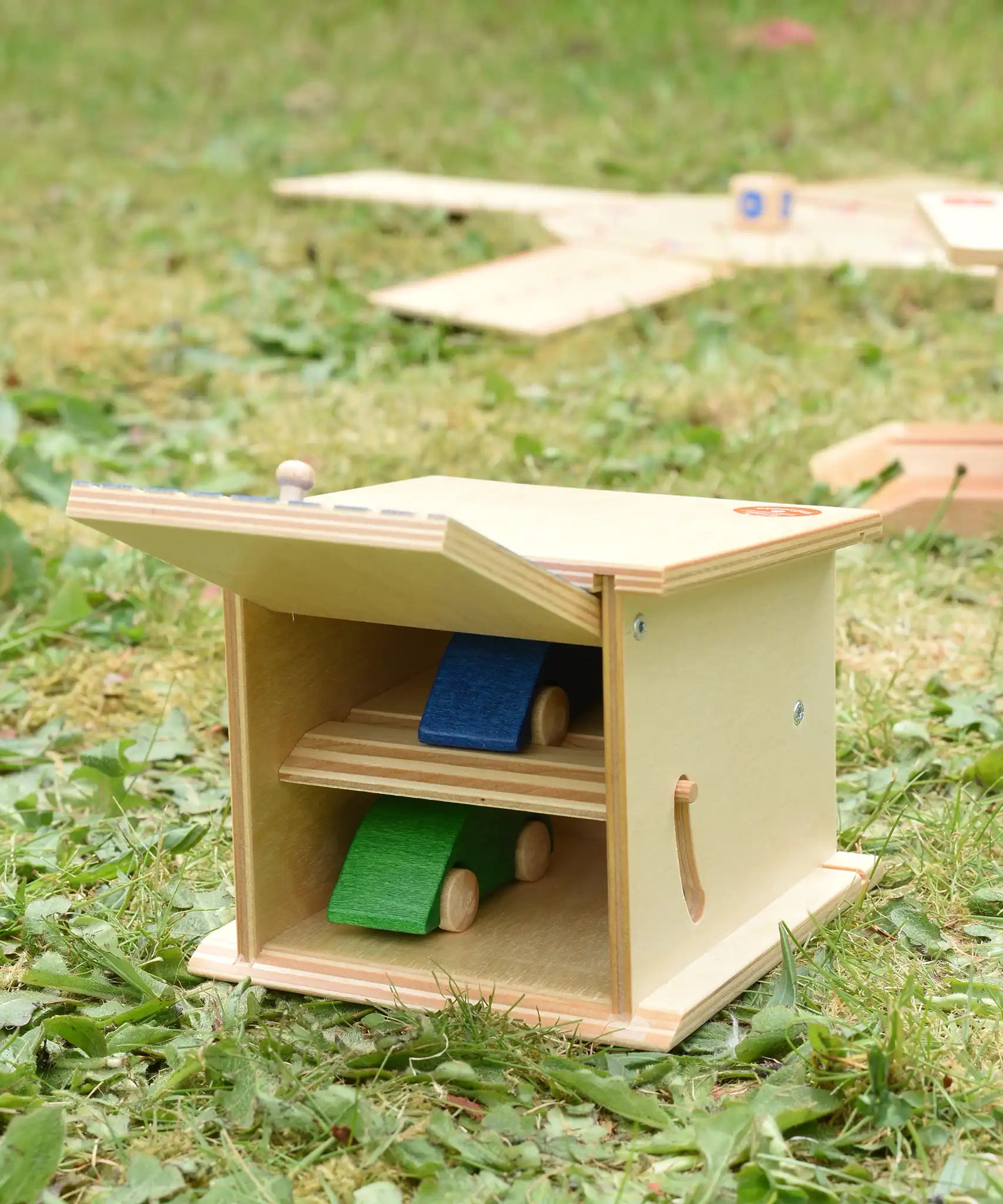 Beck wooden double garage toy with two toy cars placed inside, one on each floor. Door is shown open.
