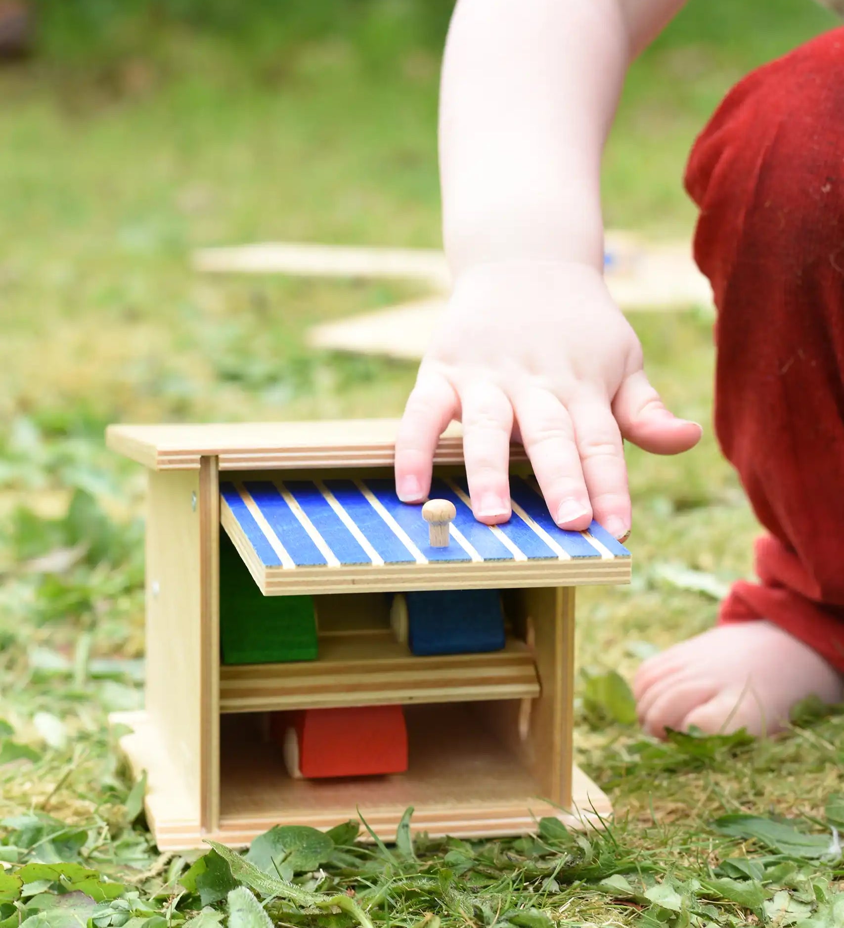 Beck wooden double garage toy played with by a child with three wooden cars paced inside.