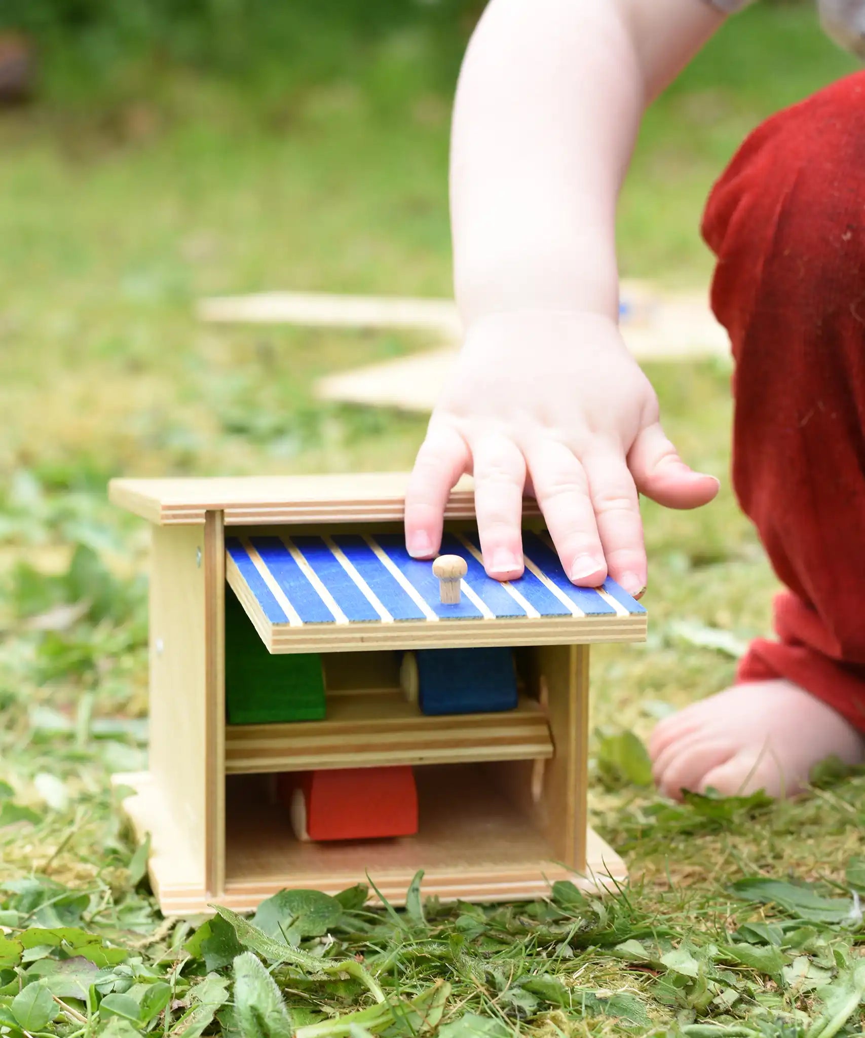 Beck wooden double garage toy played with by a child with three wooden cars paced inside.