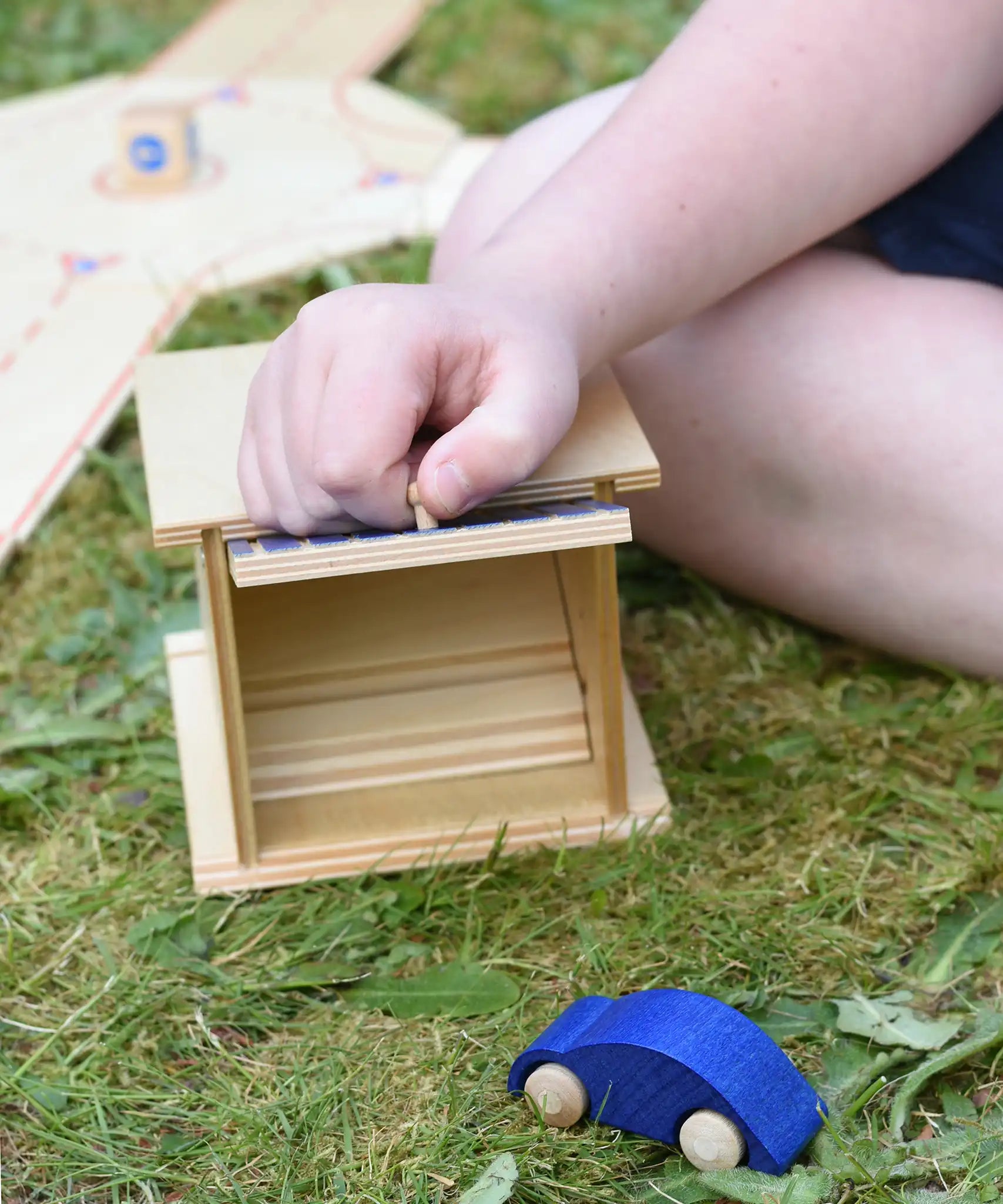 Beck wooden double garage toy placed in a small world set up. Child lifting the door by the handle.
