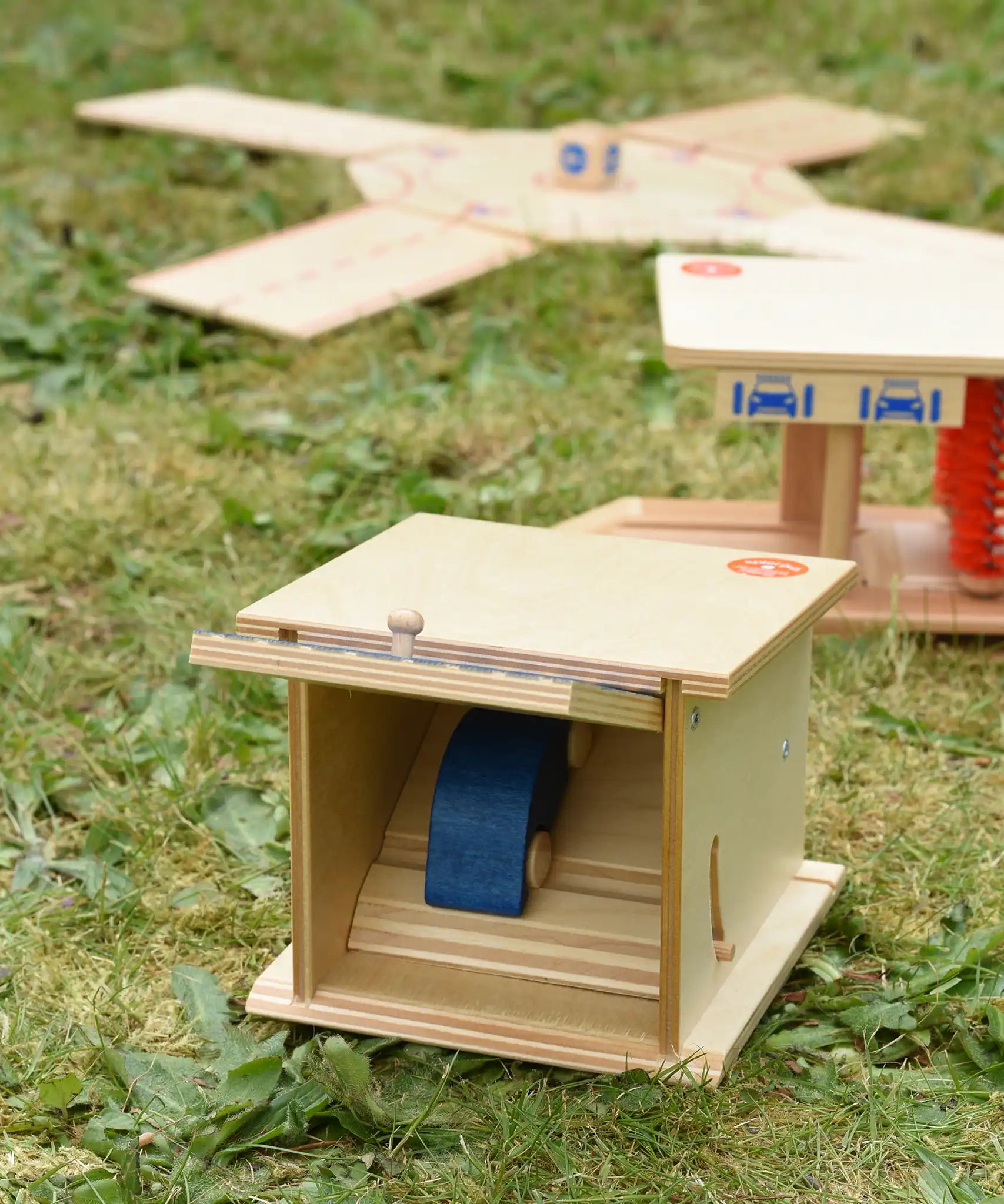 Beck wooden double garage toy placed in a small world set up with a boy car placed on the top level.