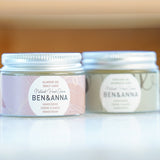 Close up of Ben & Anna sustainable natural oil hand creams on a white marble floor in front of a wooden background