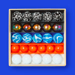 Close up of the Billes & Co colourful mini glass space mission marbles in their box on a blue background