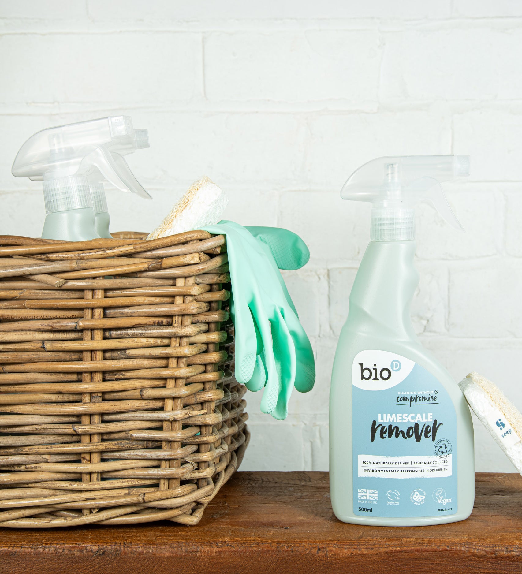 A bottle of Bio-D limescale remover standing on a wooden surface next to a wooden cleaning basket. This limescale remover is available at Babipur. 