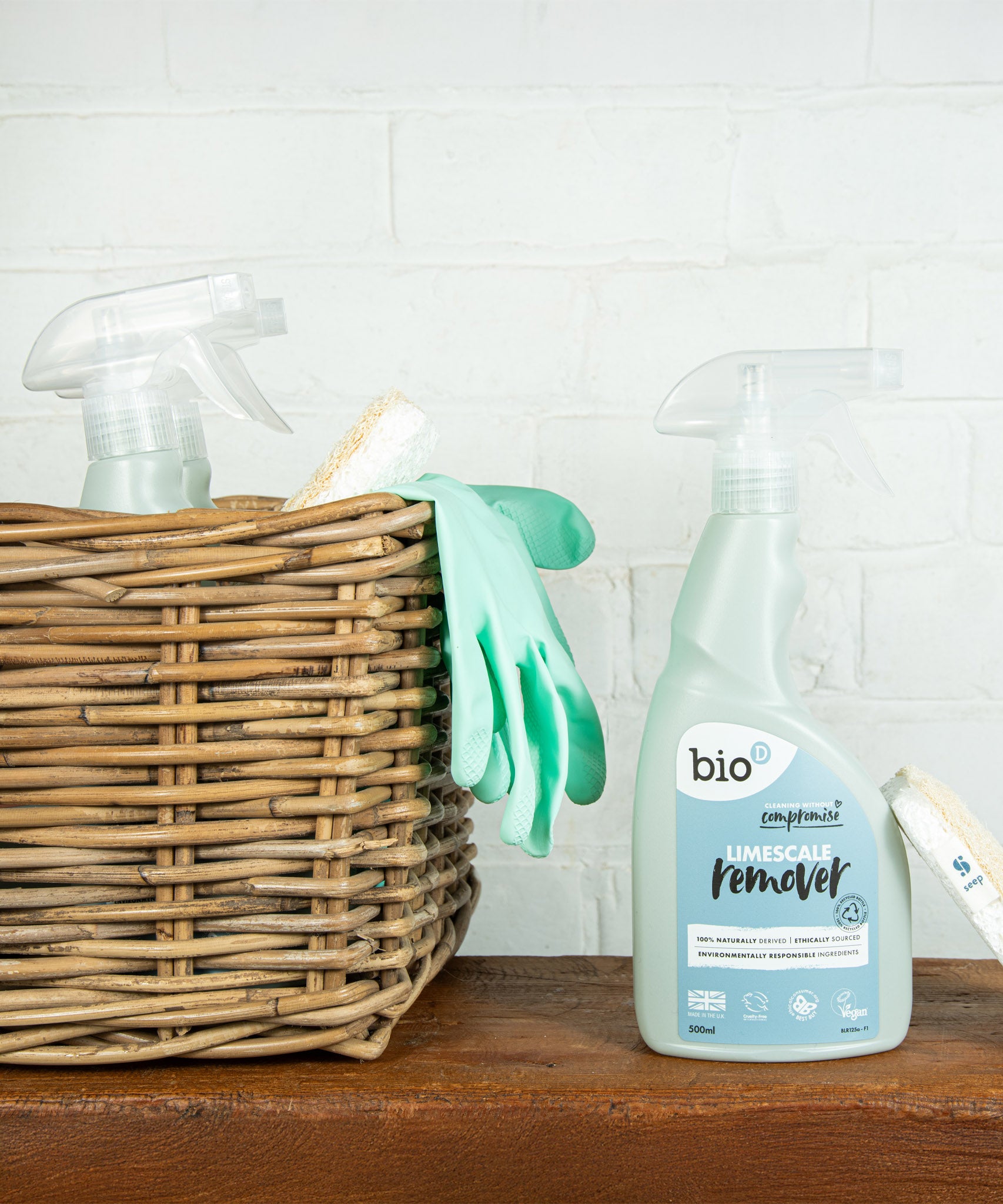 A bottle of Bio-D limescale remover standing on a wooden surface next to a wooden cleaning basket. This limescale remover is available at Babipur. 