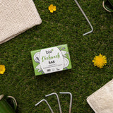 A bar of Bio-D dish washing soap inside it's green box lying on top of grass with various camping items. This dish soap bar is available at Babipur. 