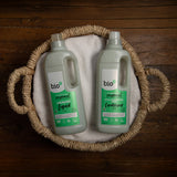 A 1L bottle of Bio-D fresh juniper fabric conditioner  and laundry liquid laying flat inside a washing basket. Both cleaning products available at Babipur. 