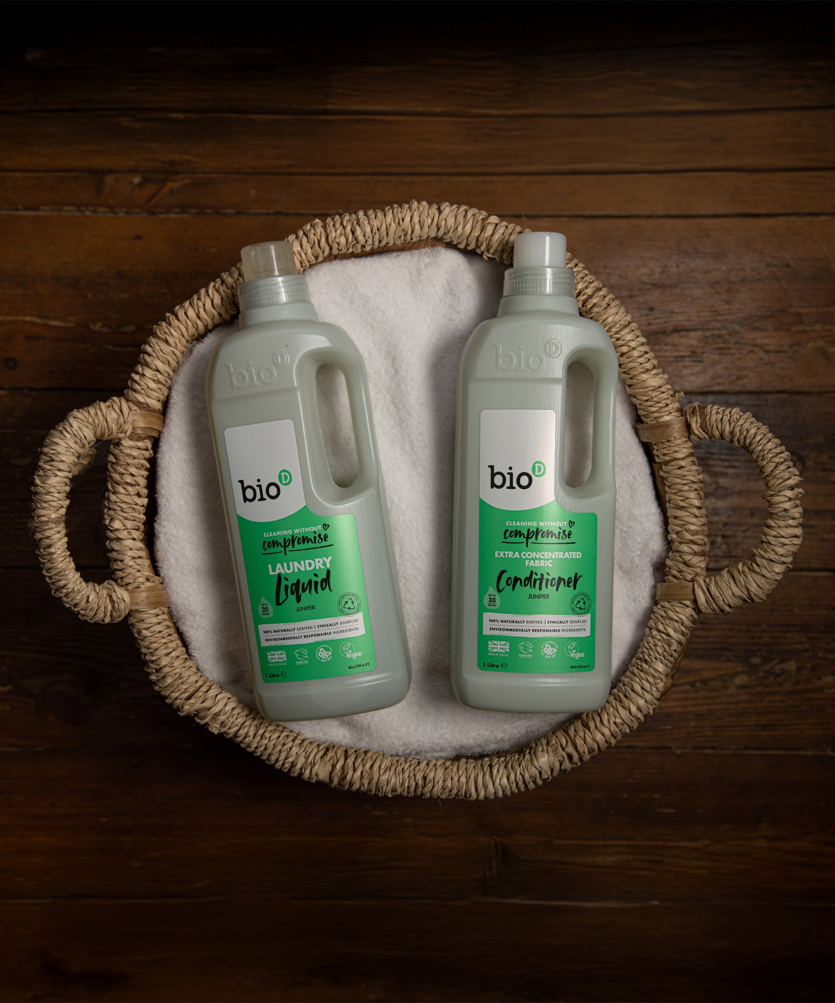 A 1L bottle of Bio-D fresh juniper fabric conditioner  and laundry liquid laying flat inside a washing basket. Both cleaning products available at Babipur. 