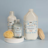 Bio-D fragrance free body wash shown alongside a bubble bath bottle and a 5 litre refill bottle, arranged with a natural sponge and loofah.