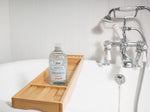 Bio-D fragrance free body wash bottle standing on a wooden bath tray beside a white bathtub with chrome taps.