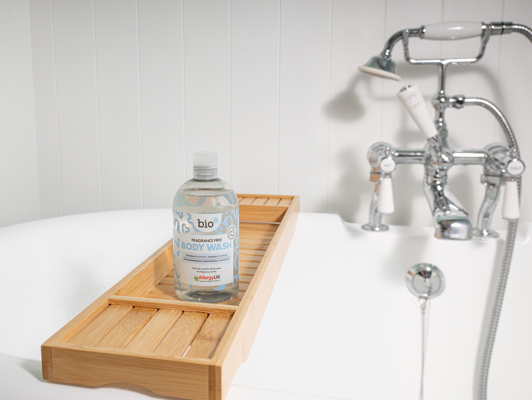 Bio-D fragrance free body wash bottle standing on a wooden bath tray beside a white bathtub with chrome taps.