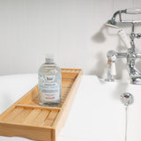 Bio-D fragrance free body wash bottle standing on a wooden bath tray beside a white bathtub with chrome taps.