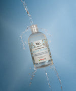 Bio-D fragrance free body wash bottle photographed mid air with water pouring and splashing through the open cap.
