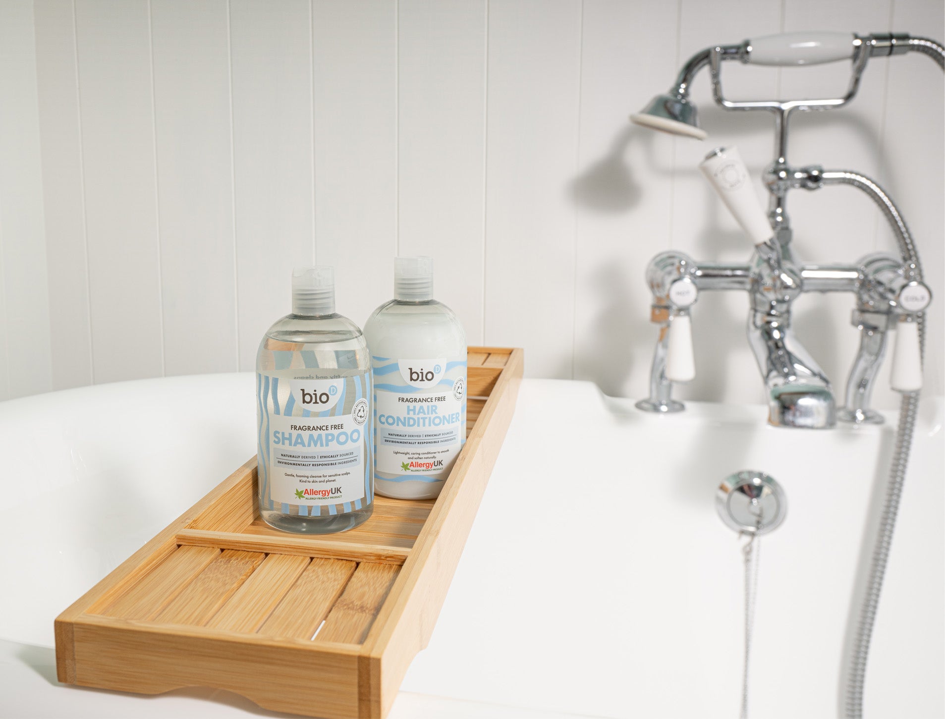 Bio-D fragrance-free shampoo and conditioner on a wooden bath tray beside a bathtub, illustrating refillable, Allergy UK approved hair care suitable for sensitive and allergy-prone skin.