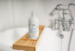 Bio-D Fragrance-Free Bubble Bath bottle placed on a wooden bath tray beside a white bathtub with chrome taps.