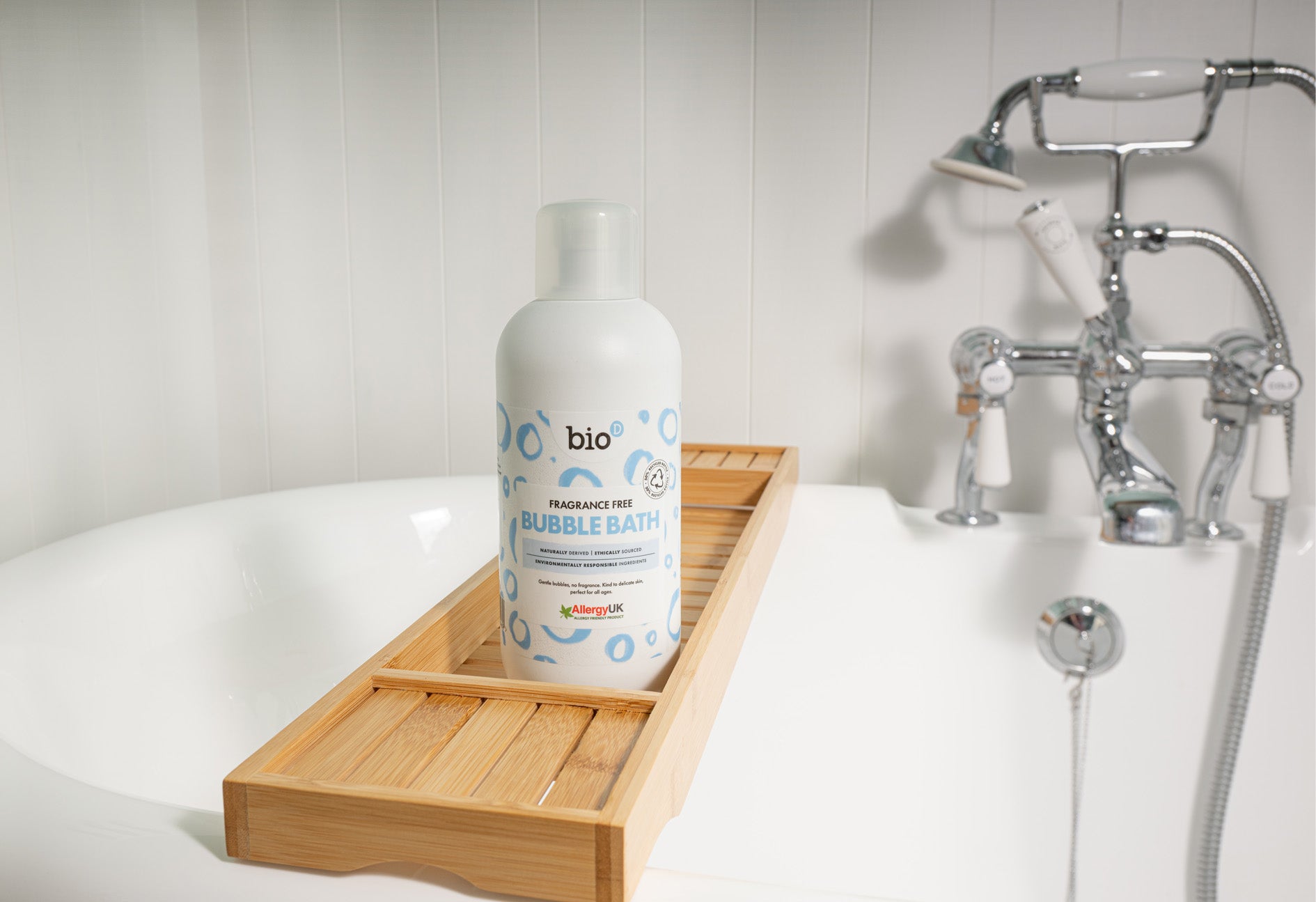 Bio-D Fragrance-Free Bubble Bath bottle placed on a wooden bath tray beside a white bathtub with chrome taps.