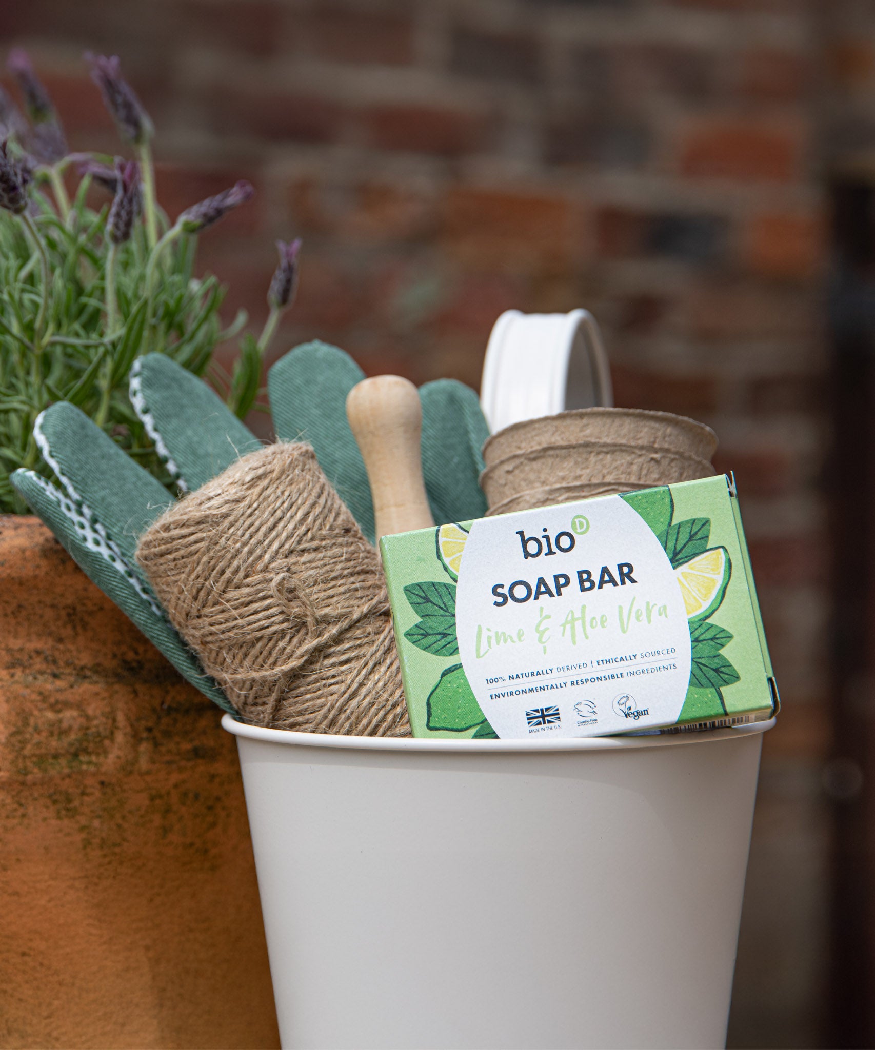 A Bio-D lime & aloe vera soap bar inside a bucket with various gardening items. This soap bar is available at Babipur