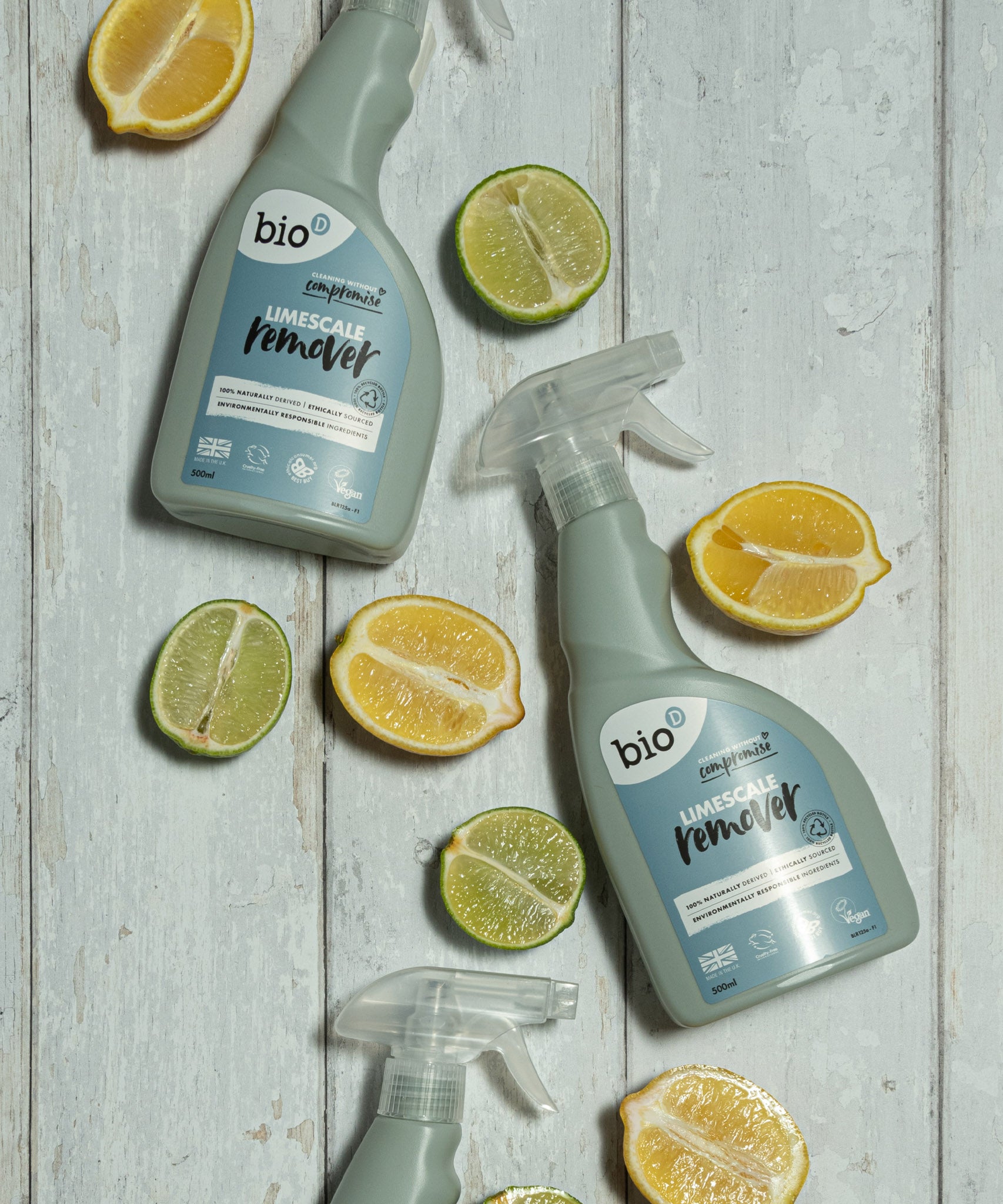 A bottle of Bio-D limescale remover lying flat on a wooden surface next to sliced fruit. This limescale remover is available at Babipur. 