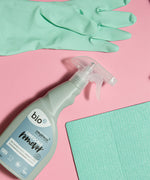 A bottle of Bio-D limescale remover lying flat on a pink background next to light green cleaning products. This limescale remover is available at Babipur. 
