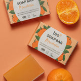 Bio-D mandarin soap bar lying next to mandarins on a light orange background. This soap bar is available at Babipur