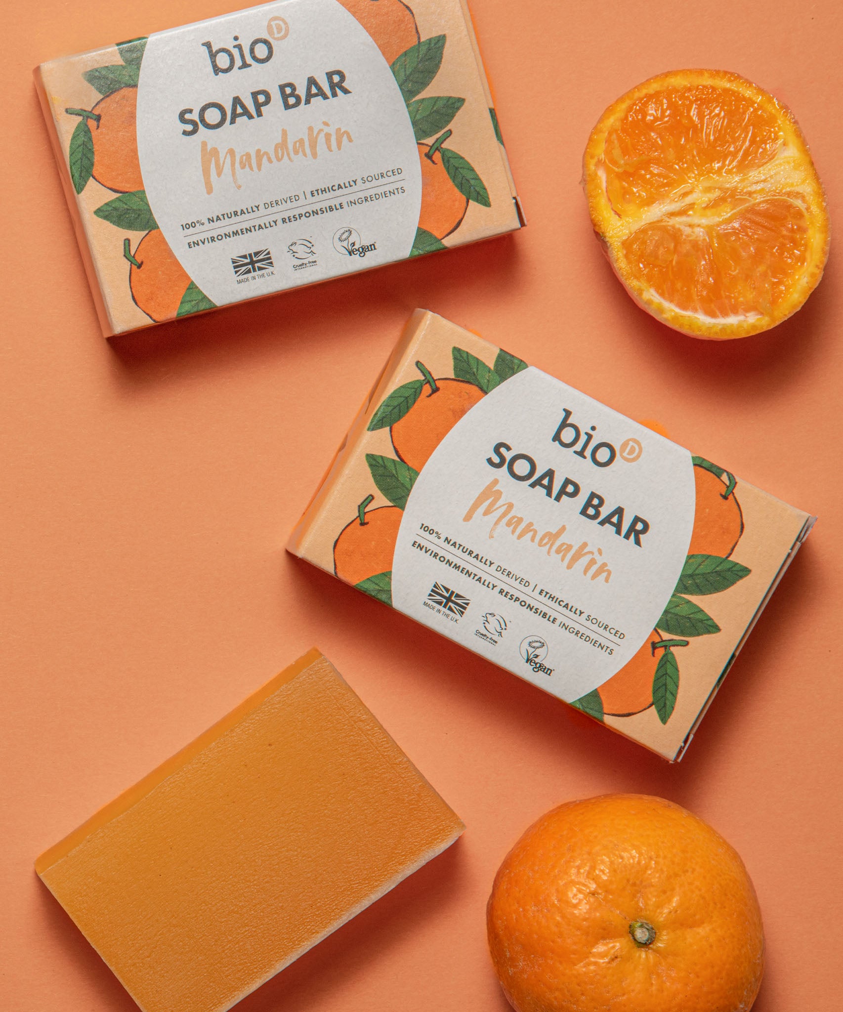Bio-D mandarin soap bar lying next to mandarins on a light orange background. This soap bar is available at Babipur