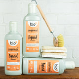 A group of Bio-D 750ml mandarin washing up liquid bottles standing on a wooden surface next to cleaning products. This washing up liquid is available at Babipur