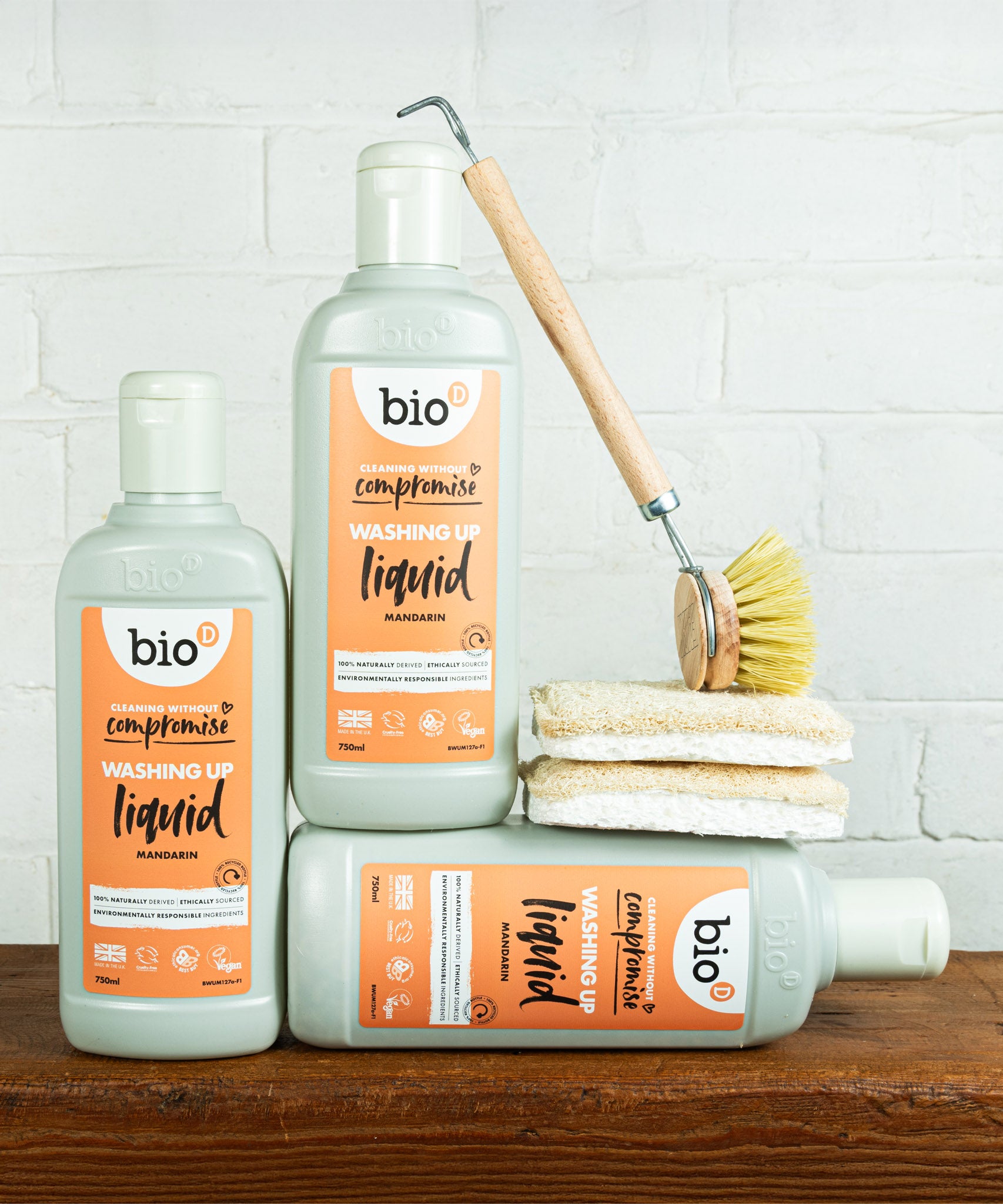 A group of Bio-D 750ml mandarin washing up liquid bottles standing on a wooden surface next to cleaning products. This washing up liquid is available at Babipur
