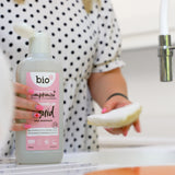 An adult holding the Bio-D pink grapefruit 750ml washing up liquid and washing the dishes. This washing up liquid is available at Babipur.