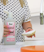 An adult holding the Bio-D pink grapefruit 750ml washing up liquid and washing the dishes. This washing up liquid is available at Babipur.