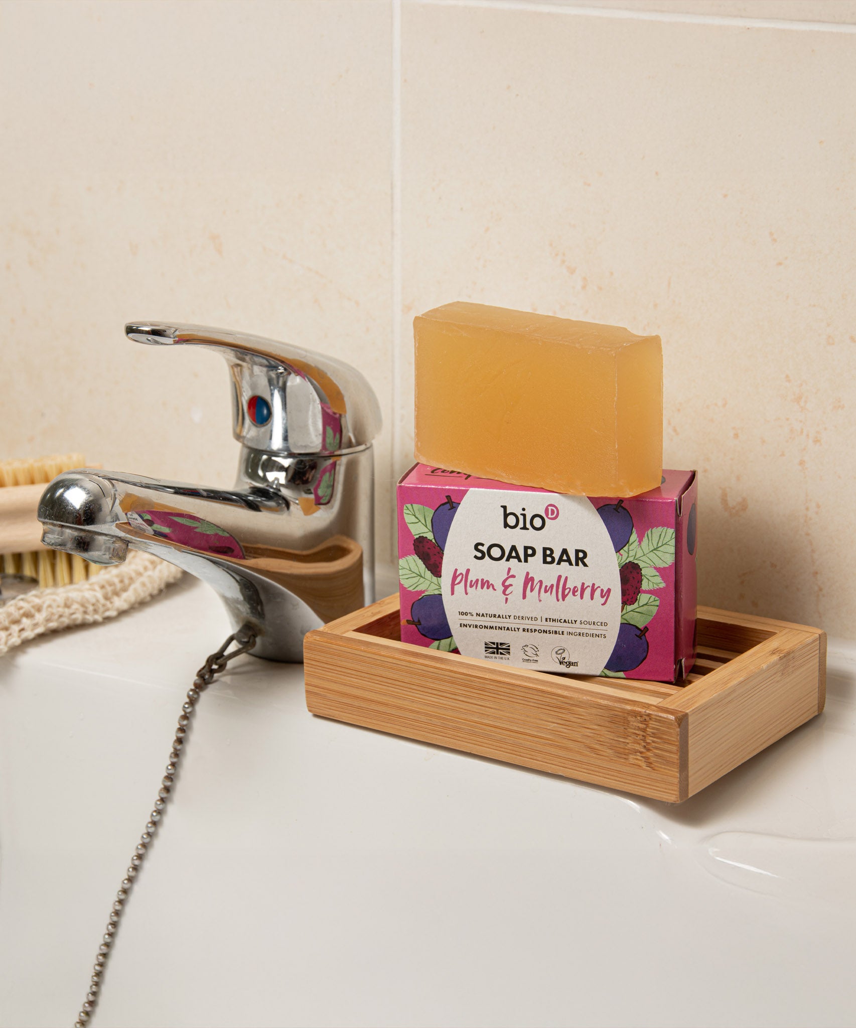 Bio-D plum & mulberry soap bar standing in a wooden soap dish on a sink. This soap bar is available at Babipur.