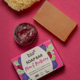 Bio-D plum & mulberry soap bar lying next to a plum and sponge on a light purple background. This soap bar is available at Babipur