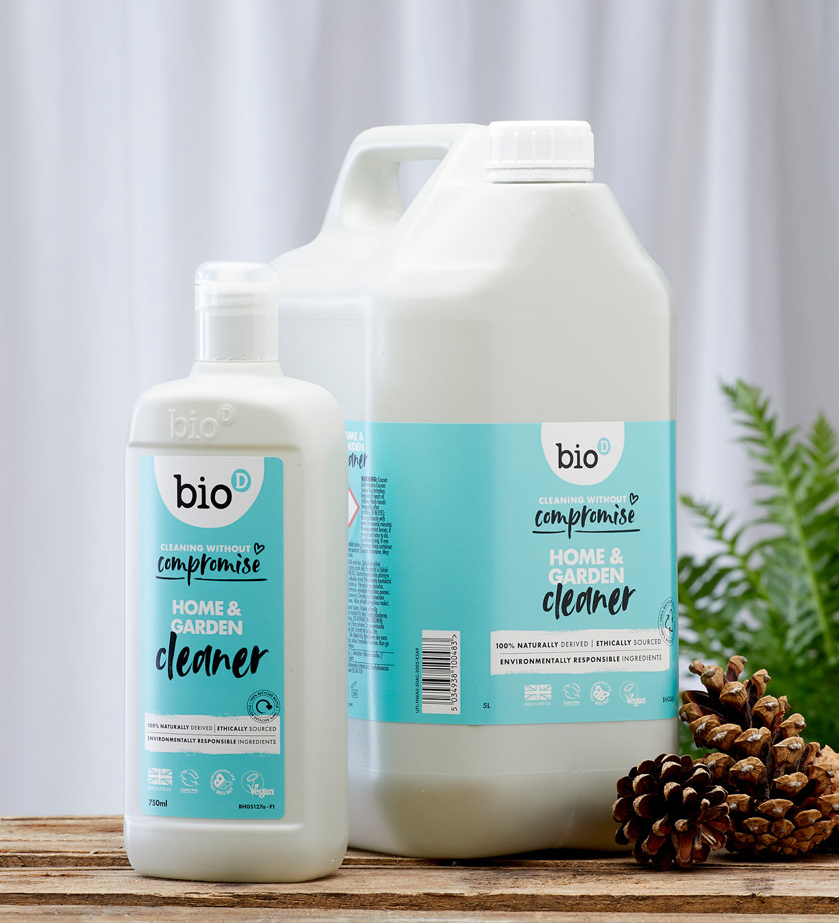 Front view of Bio-D Home and Garden Cleaner bottles in 750ml and 5 litre sizes, standing on a wooden surface with pine cones and greenery to show the refill size alongside the smaller bottle.