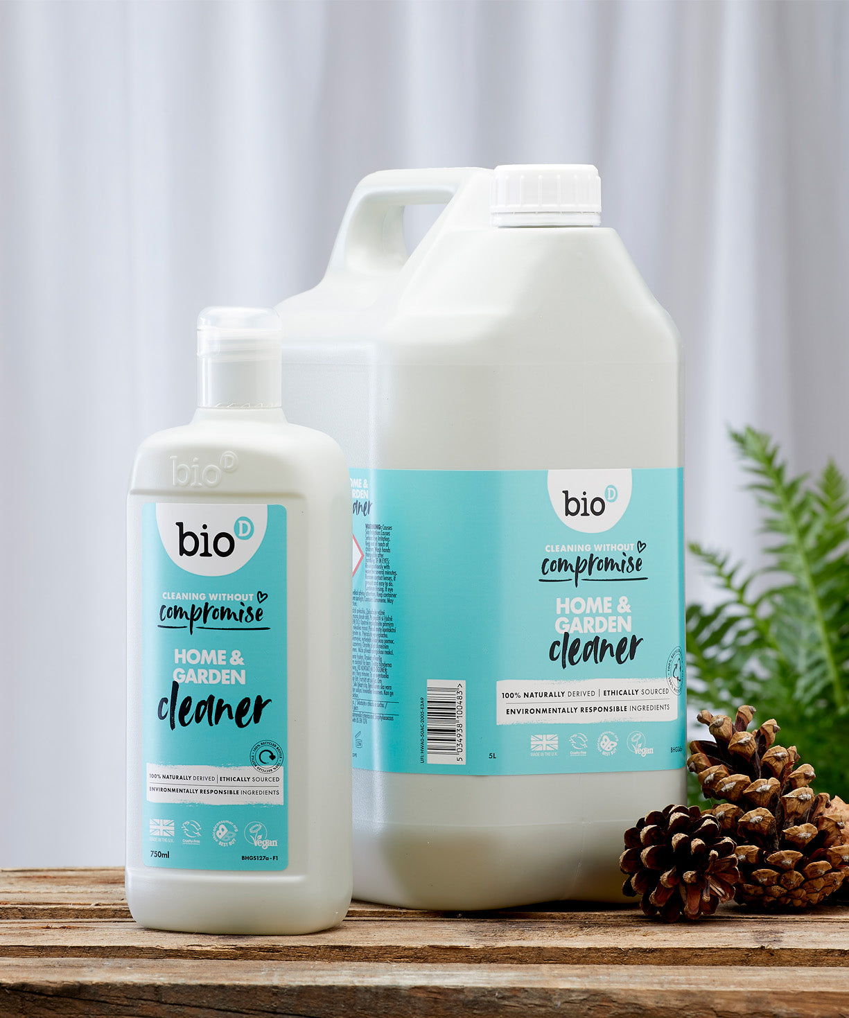 Front view of Bio-D Home and Garden Cleaner bottles in 750ml and 5 litre sizes, standing on a wooden surface with pine cones and greenery to show the refill size alongside the smaller bottle.